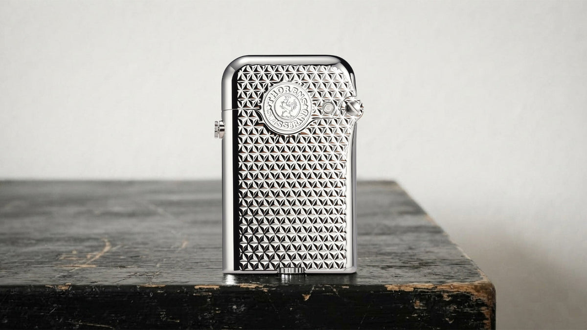 Silver THORENS lighter with textured mesh case on a dark tabletop