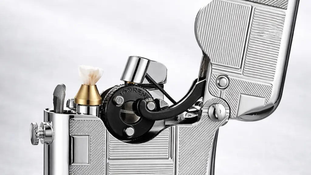 alt=Geometric engraved brass fluid lighter with exposed single-claw ignition and side refill system