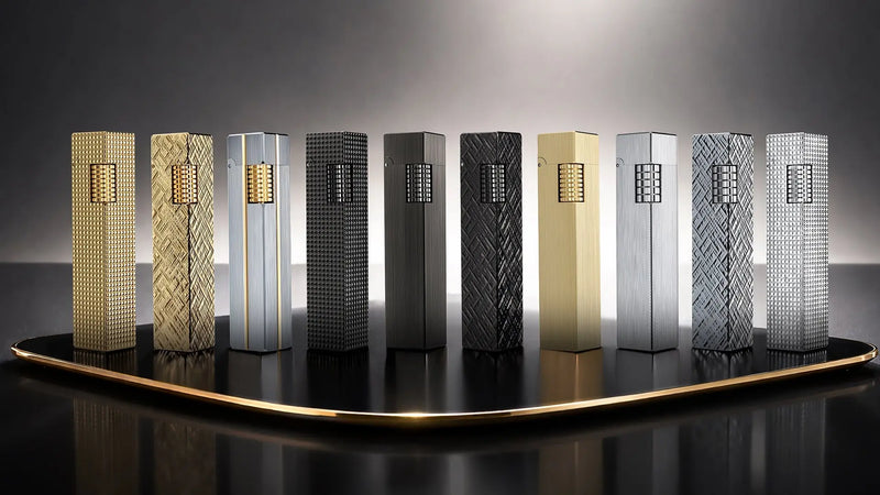 Lineup of THORENS Rectangular Series fluid lighters displayed on a dark presentation platform, featuring rectangular designs in gold-tone, silver-tone, and black metal finishes with different engraved textures.