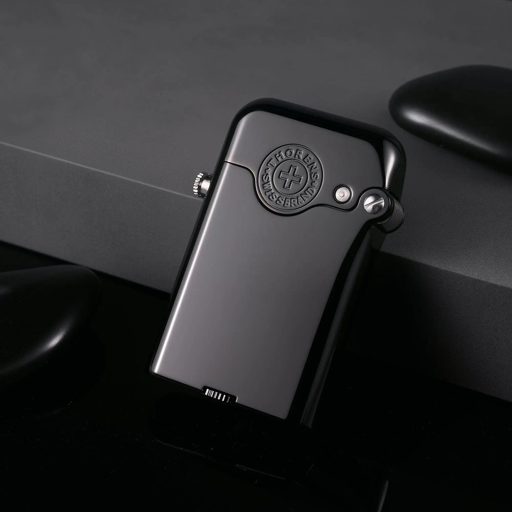 Perspective view of the Thorens Gen 3 glossy black lighter leaning against a textured gray block, highlighting its curved edges, embossed Swiss emblem, and reflective metallic finish.