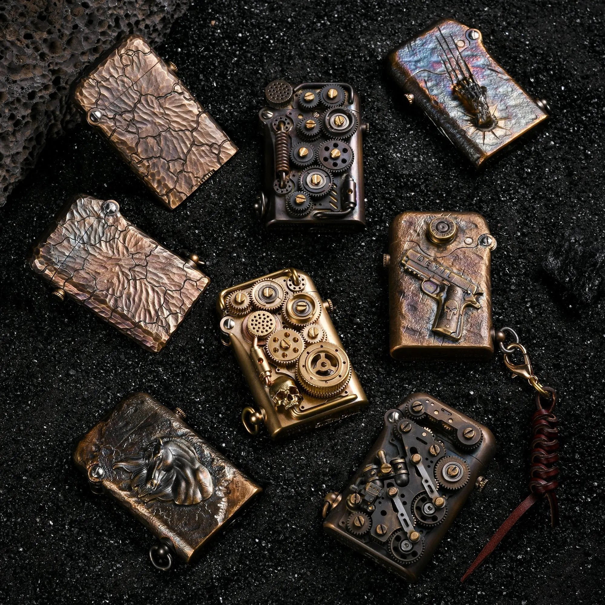 A curated selection of Gen 1 Single Claw lighters, including the hand-carved Earth Fissure models, steampunk gear designs, and relief sculptures, displayed on black volcanic sand.