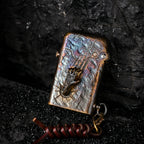A Gen 1 Single Claw Spirit Claw lighter featuring a 3D skeletal hand relief and iridescent heat-treated brass, resting against dark volcanic rock.