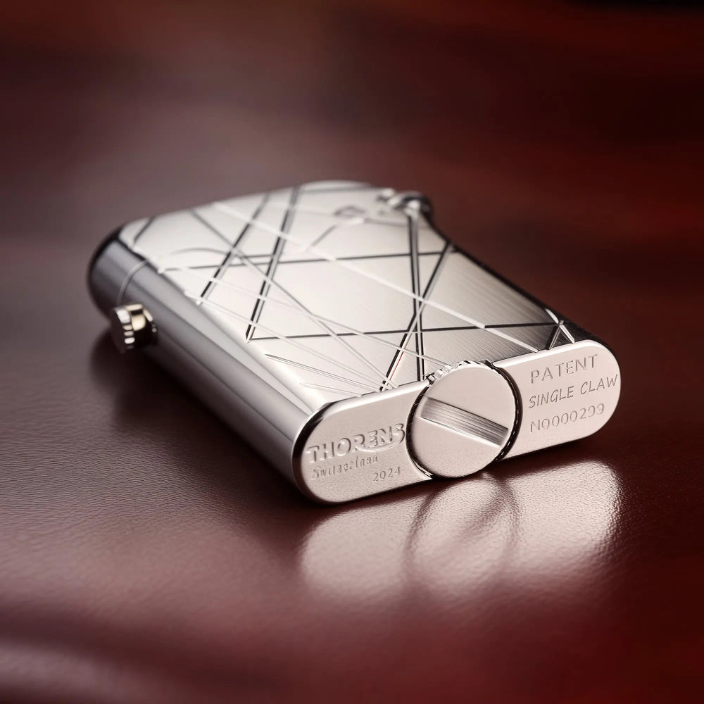 A close-up view of a silver Thorens Gen 3 Single Claw lighter with a geometric modern grid pattern, resting on dark leather, showcasing the base markings.
