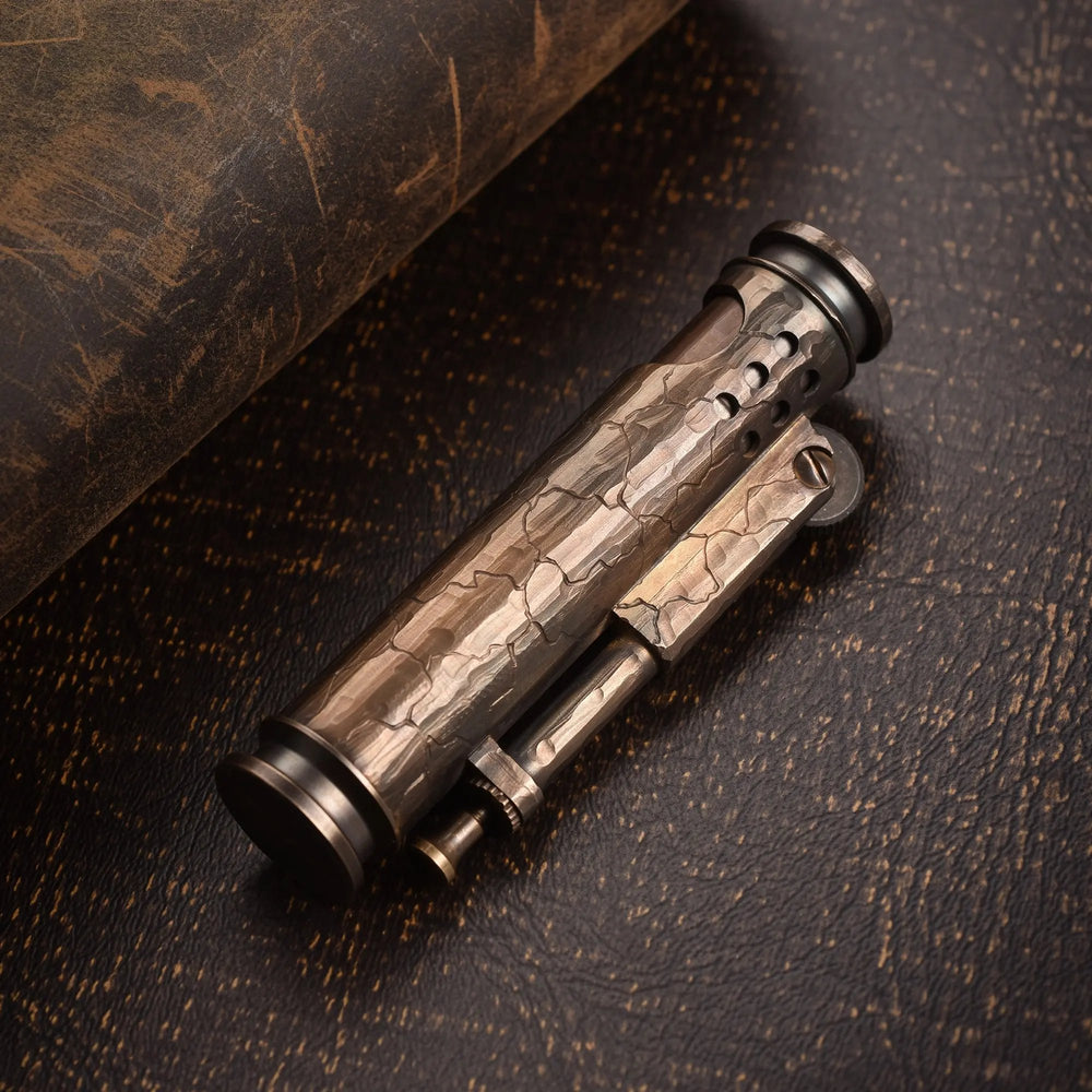 A cylindrical Battle Soul trench lighter featuring hand-carved cracks and a weathered brass finish, resting on a rustic dark leather surface.