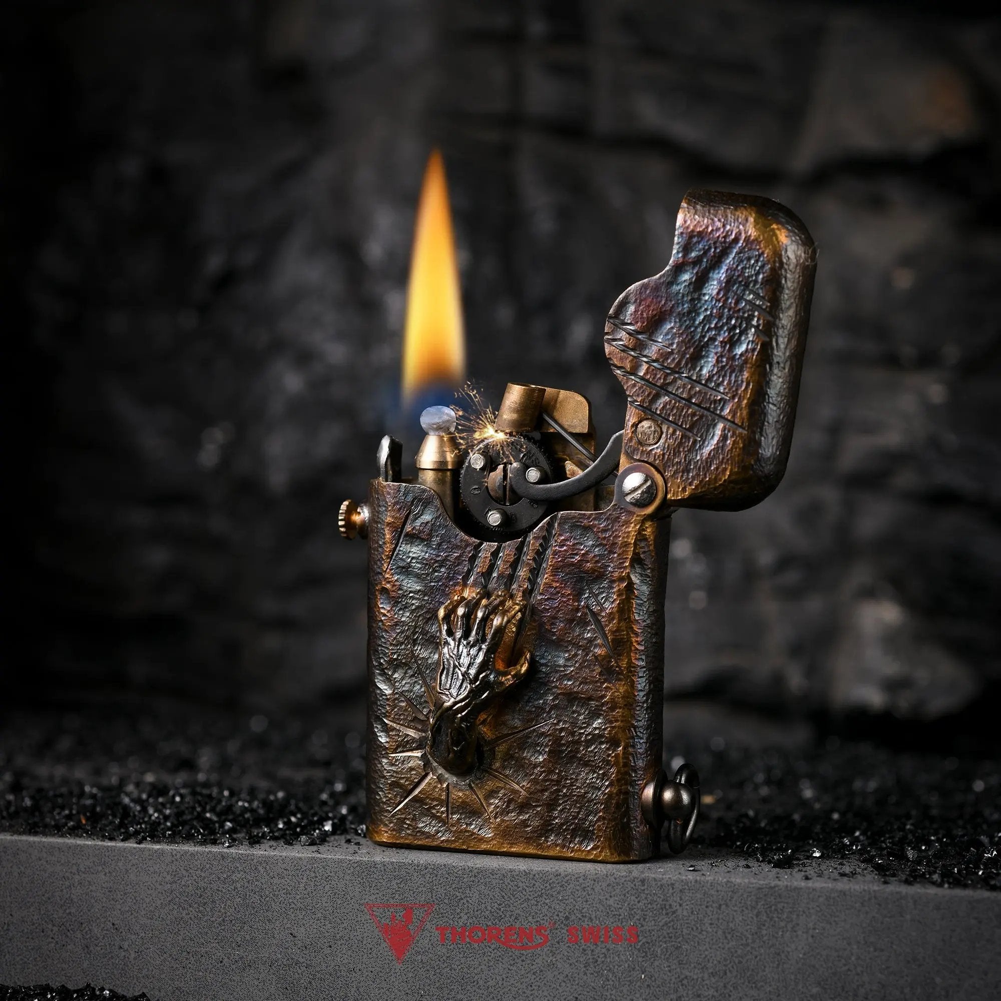 An ignited Gen 1 Single Claw Spirit Claw lighter, showing the mechanical gear spark and flame alongside its rugged hand-carved skeletal relief.