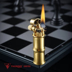 A brushed brass Mini Bamboo lighter producing a steady flame and visible ignition sparks, positioned on the edge of a silver and black chessboard with the Thorens Swiss logo in the foreground.