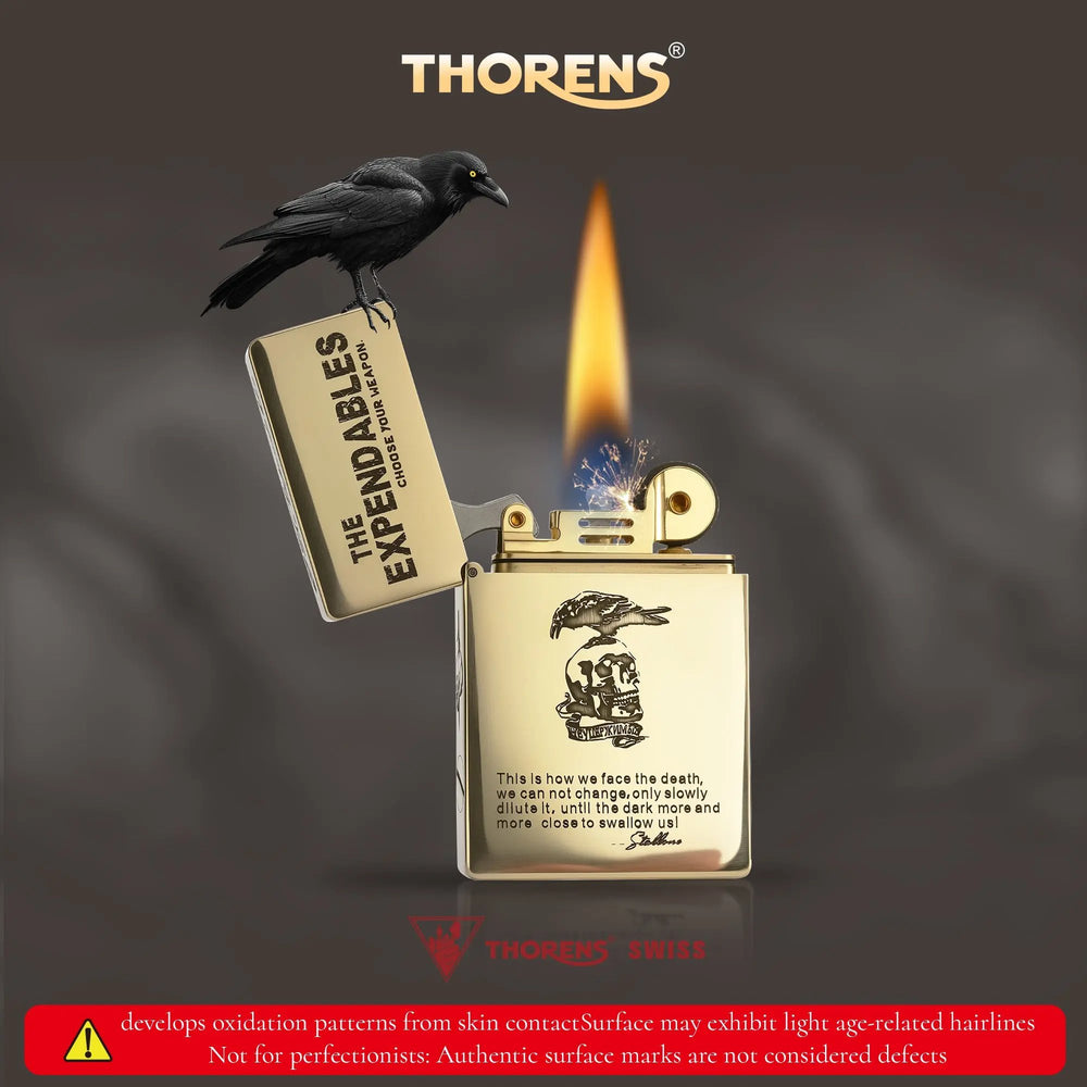 Lit Thorens brass lighter featuring THE EXPENDABLES etched logo and a perched crow, with a warning note about authentic brass oxidation patterns.