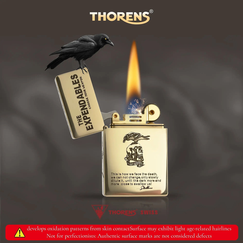 Lit Thorens brass lighter featuring THE EXPENDABLES etched logo and a perched crow, with a warning note about authentic brass oxidation patterns.
