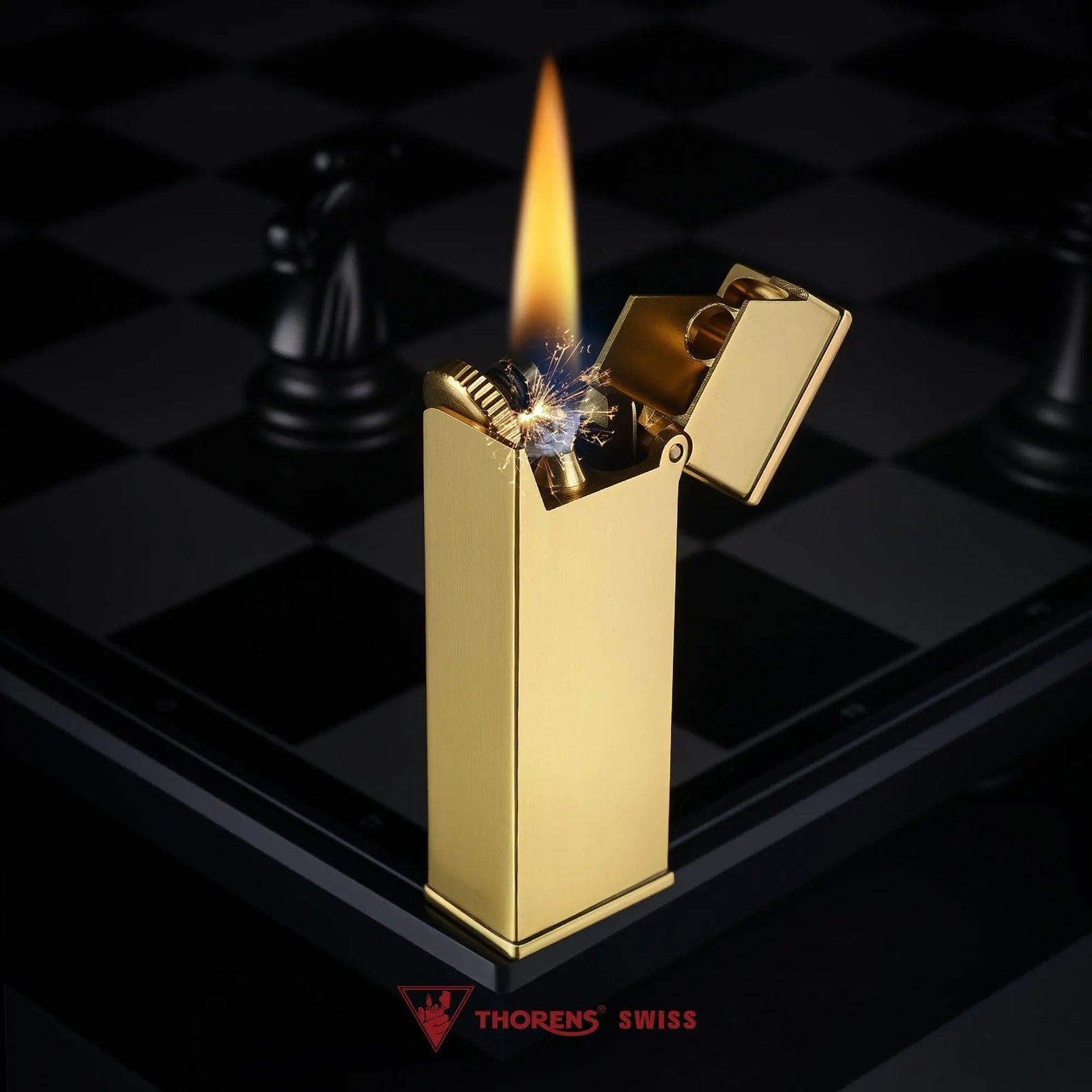 A brushed brass Long Fellow lighter ignited on a chessboard, featuring an active flame, mechanical sparks, and an open flip-top cap showing its Swiss craftsmanship.