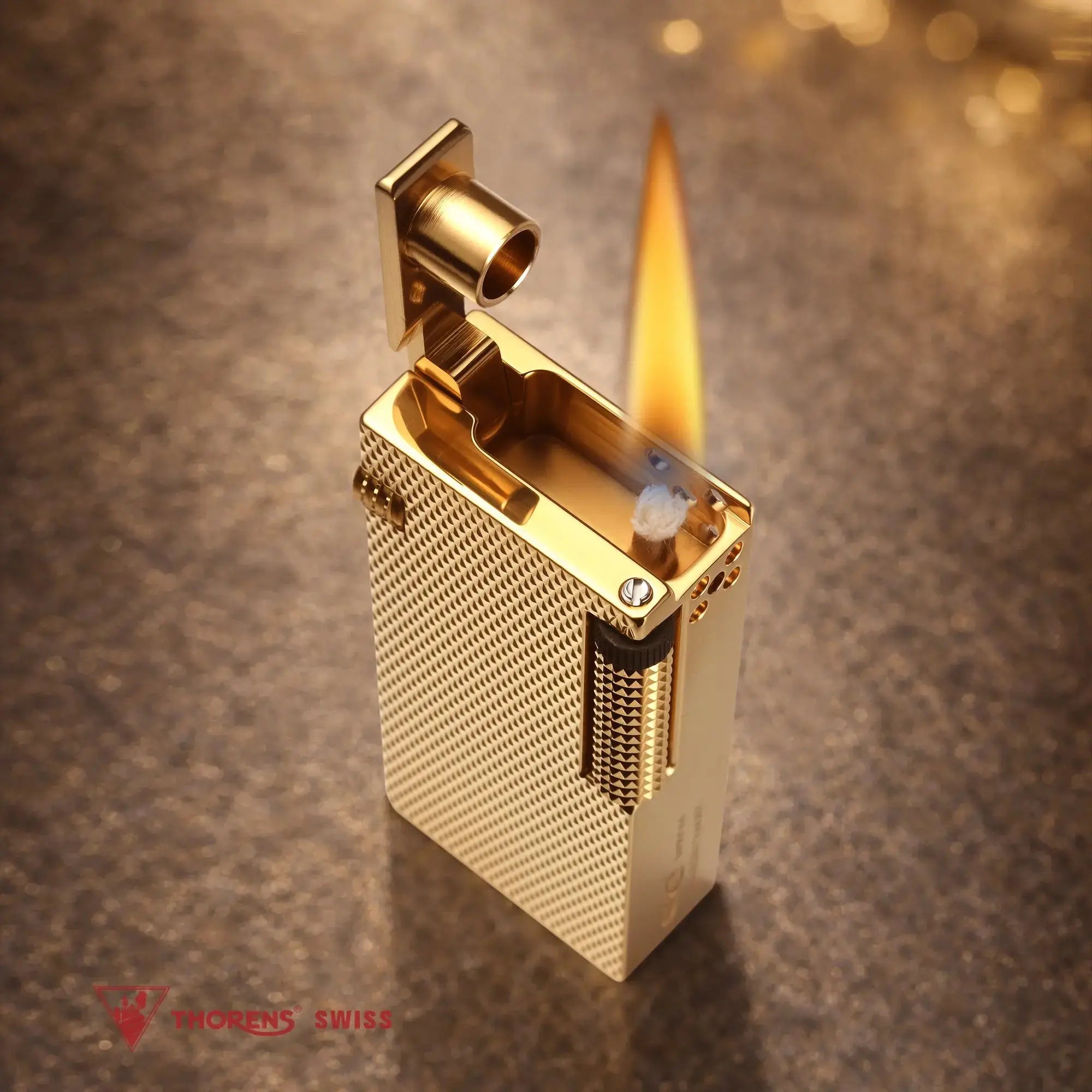Thorens Slim Cube Golden Mesh lighter shown lit on a softly textured surface, featuring a slim rectangular form, golden mesh texture, polished gold-tone body, and refined mechanical detailing