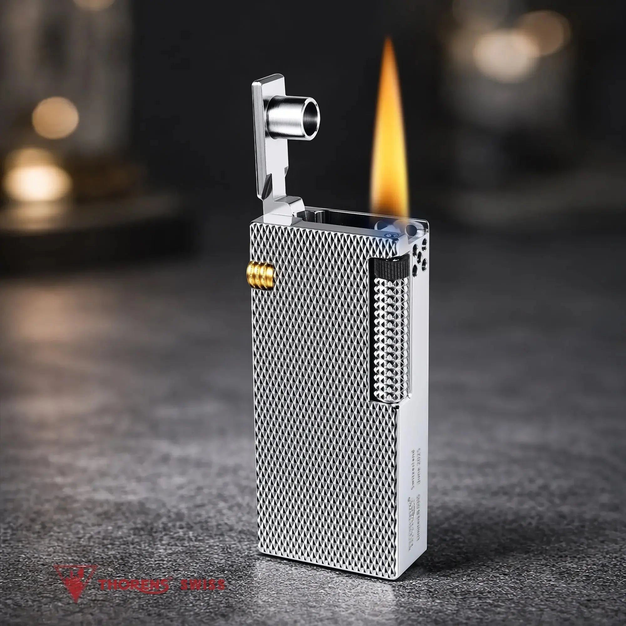 Thorens Slim Cube Silver Mesh lighter shown lit on a softly textured surface, featuring a slim rectangular form, silver mesh finish, polished silver-tone body, and gold-tone accent detail