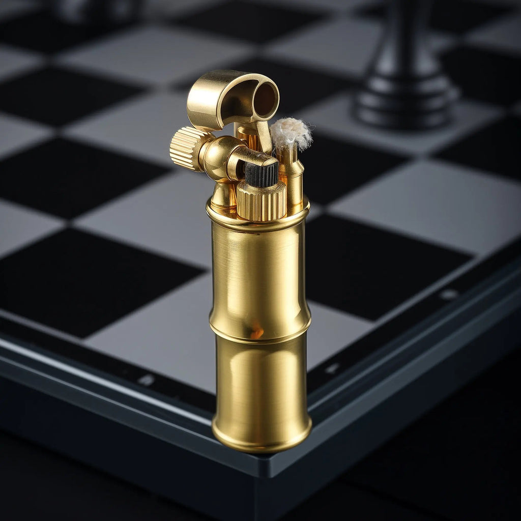 A vertical close-up of the Mini Bamboo brass lighter on a silver and black chessboard, showing the snuffer cap flipped open to reveal the cotton wick and mechanical ignition assembly.