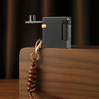 Thorens Mini Cube Black Mesh lighter displayed on a wood surface, featuring its compact square form, textured black mesh finish, side flint wheel, gold-tone accent, and leather lanyard with clasp against a warm dark background