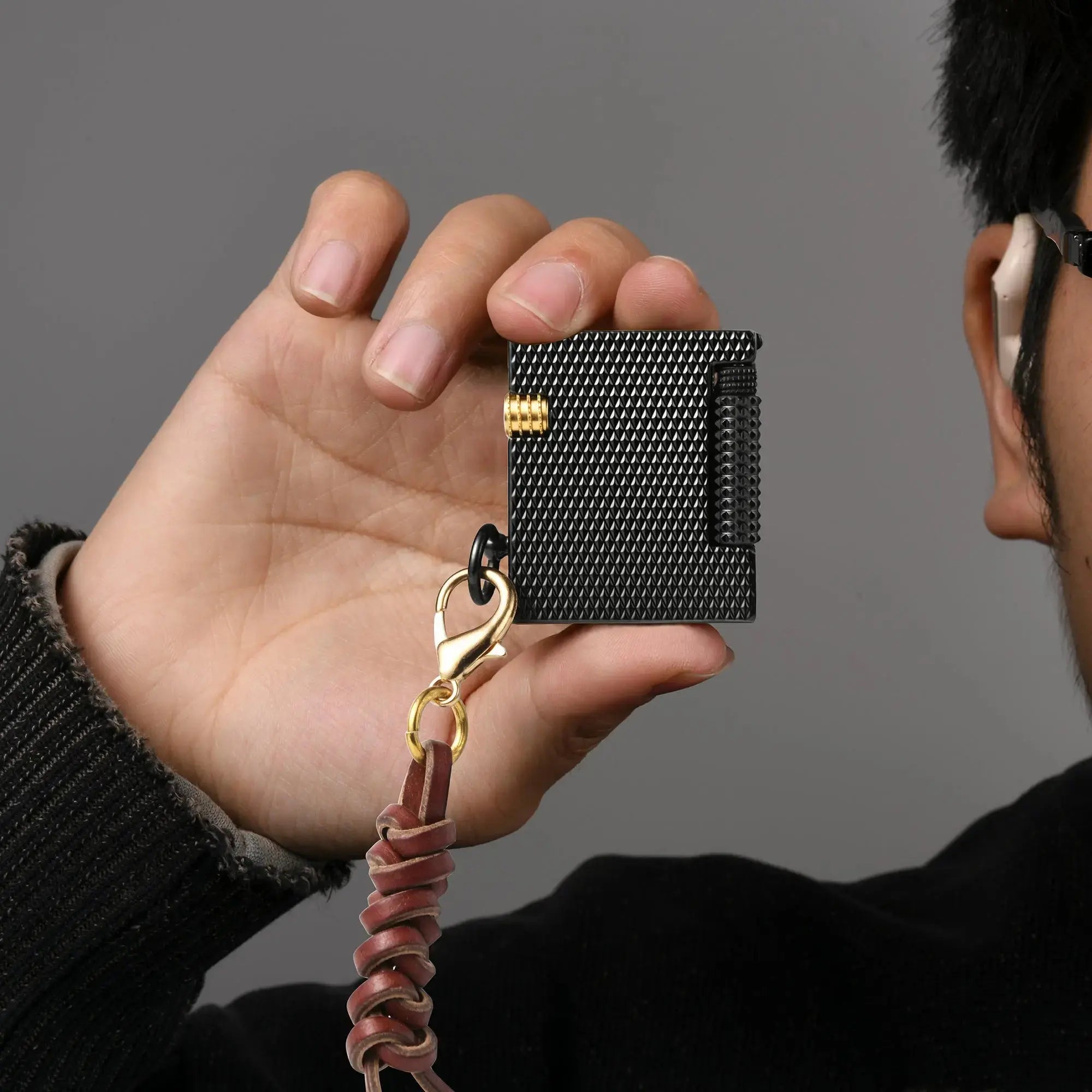 Thorens Mini Cube Black Mesh lighter held in hand, showing its compact square form, textured black mesh finish, gold-tone accent, and leather lanyard against a neutral background