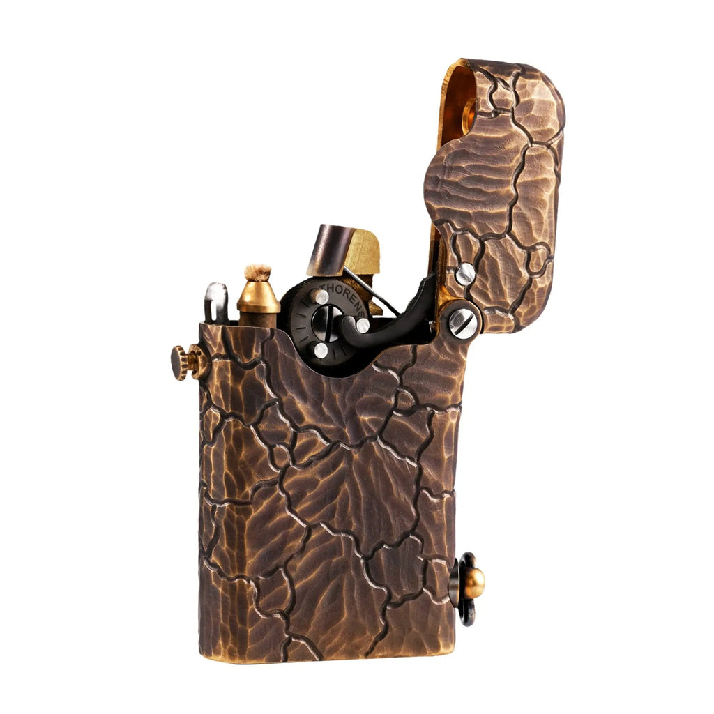 A side profile of an open Gen 1 Single Claw lighter, showcasing the deep hand-carved Earth Fissure texture on a weathered brass body against a white background.