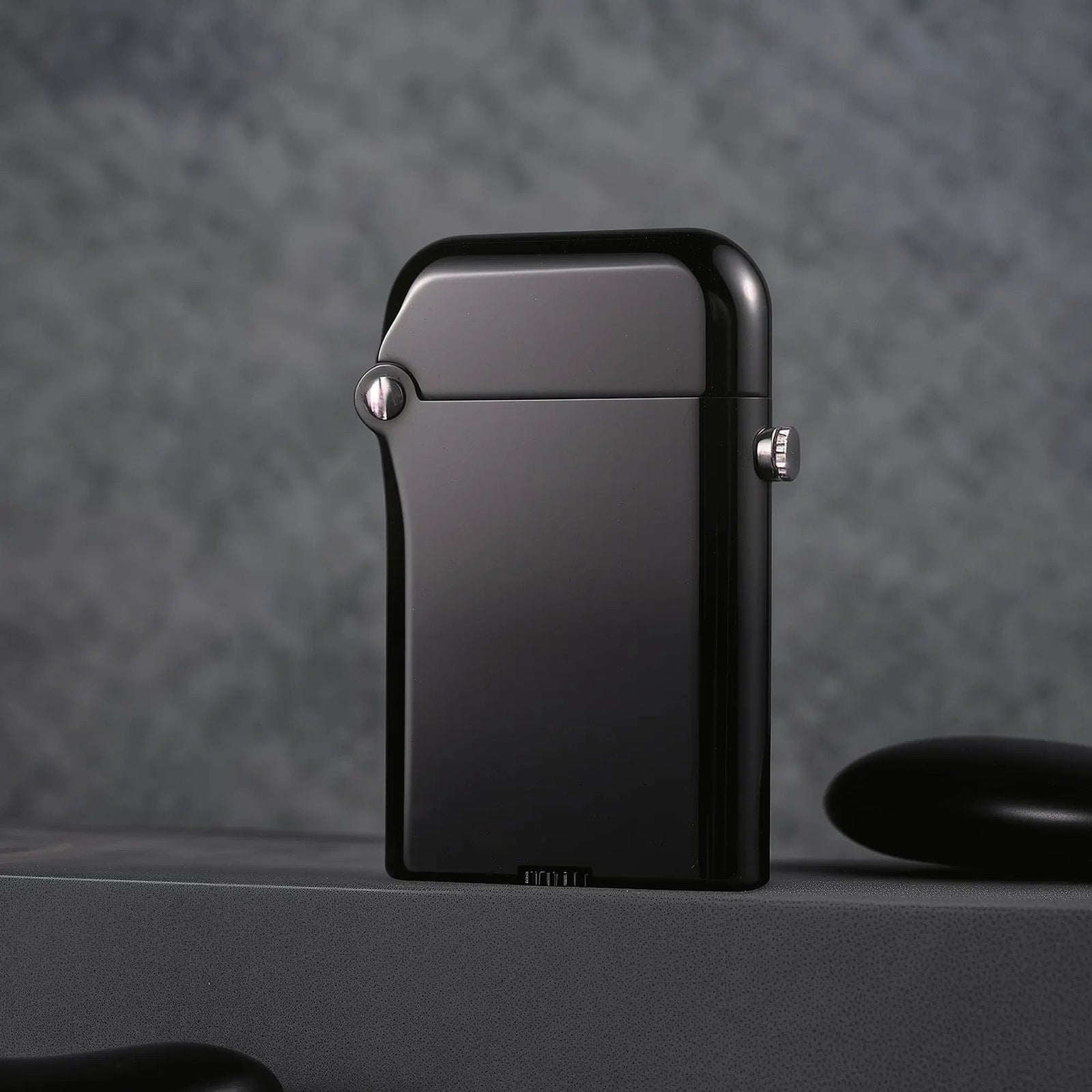 Minimalist back view of the Thorens Gen 3 glossy black lighter, showcasing its smooth mirror-like finish and precision silver hinge pin against a dark, moody background.