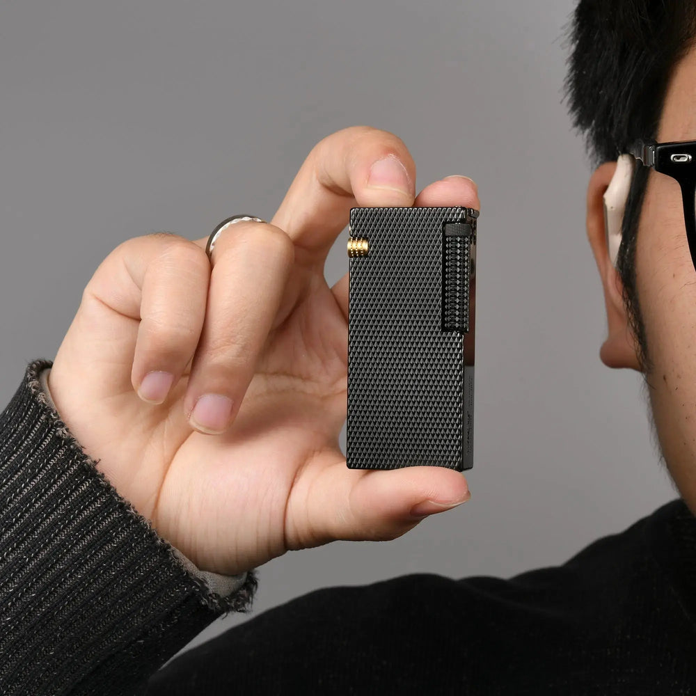 Thorens Slim Cube Black Mesh lighter held in hand, showing its slim rectangular form, black mesh finish, dark-toned body, and gold-tone accent against a neutral background