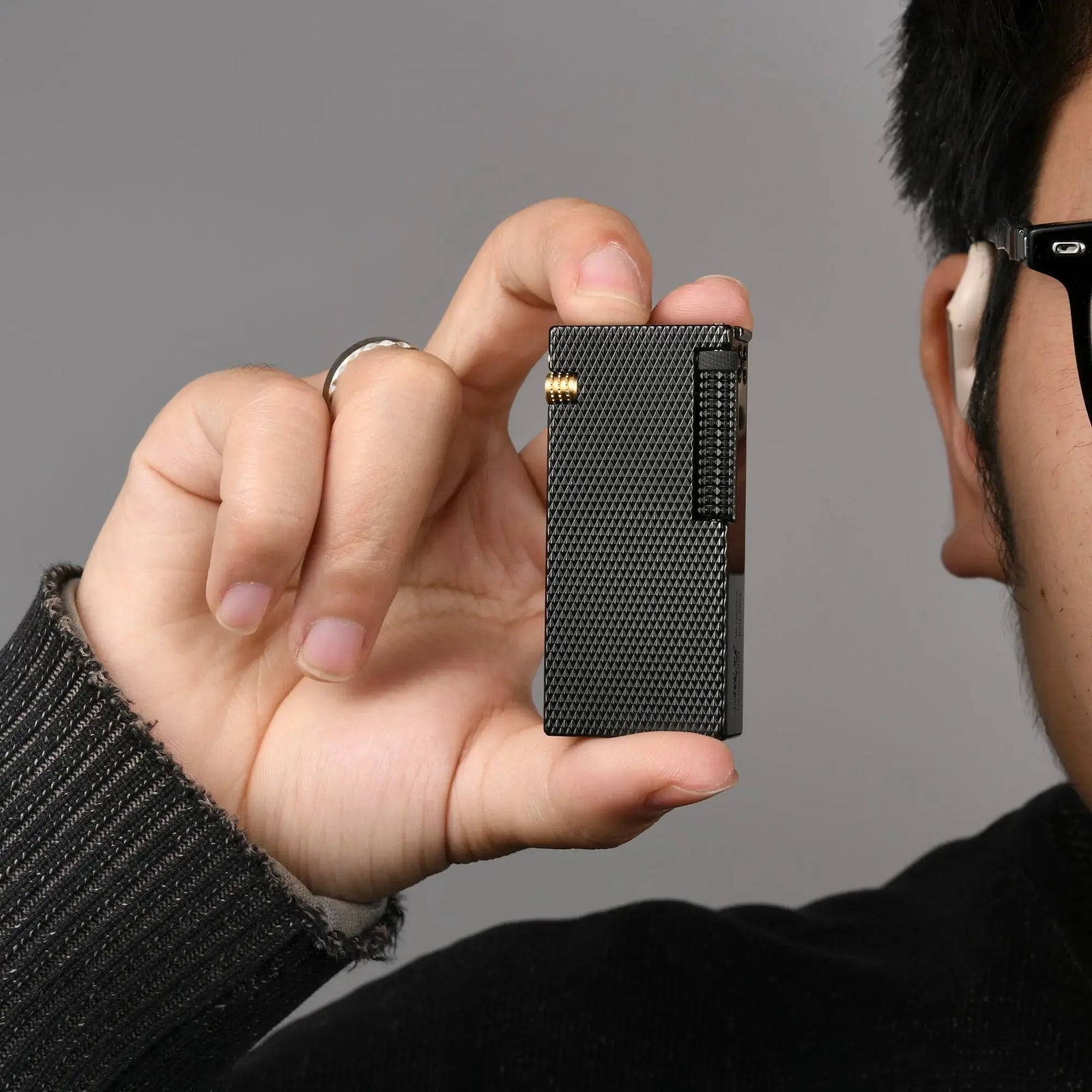 Thorens Slim Cube Black Mesh lighter held in hand, showing its slim rectangular form, black mesh finish, dark-toned body, and gold-tone accent against a neutral background