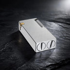 Thorens Slim Cube Silver Mesh lighter resting on a dark textured surface, featuring a refined rectangular form, silver mesh pattern, polished silver-tone body, and gold-tone accent detail