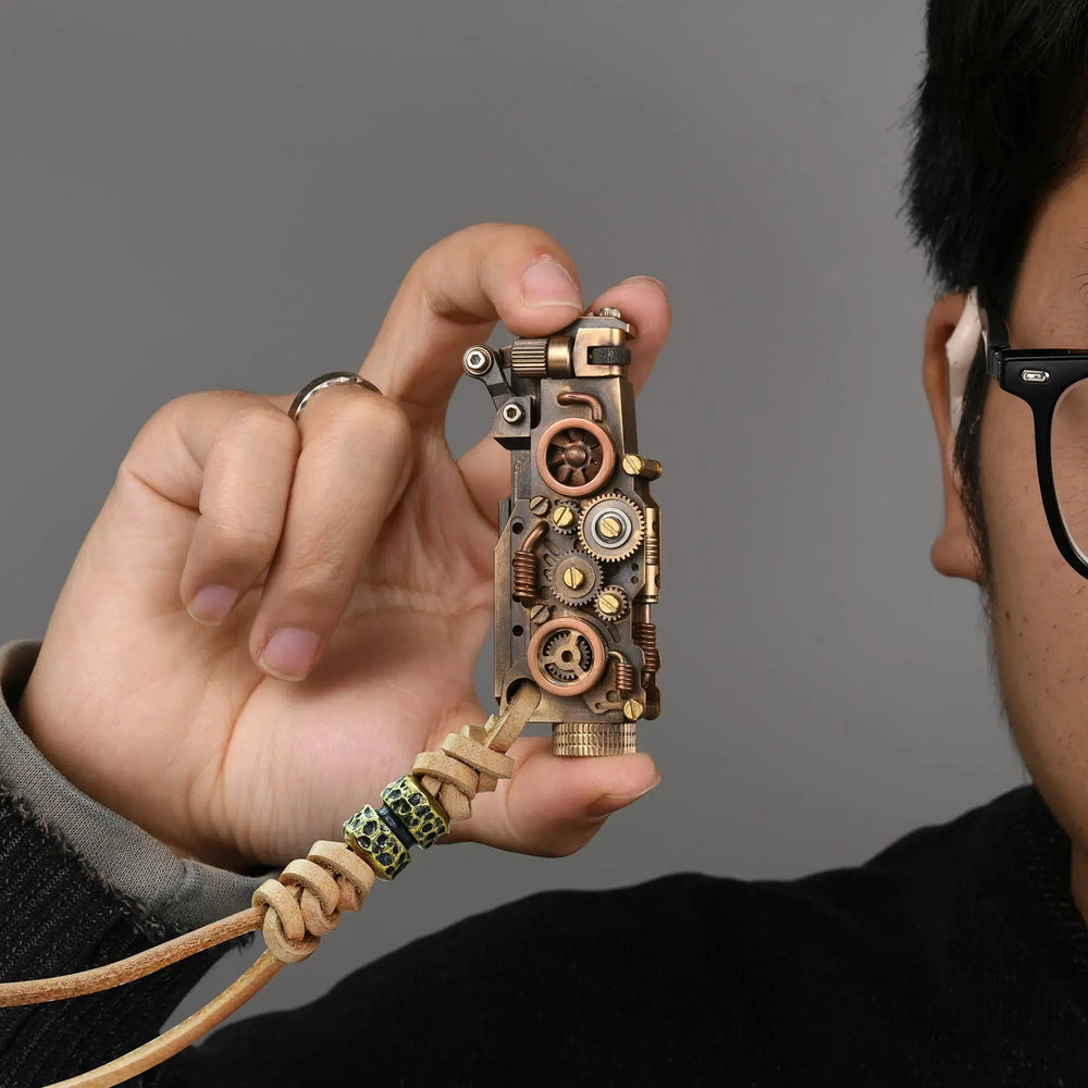 Thorens steampunk mechanical grip lighter in antique bronze held in hand, featuring exposed fine gear detailing, mixed metal tones, and a leather lanyard with bead accents against a neutral background