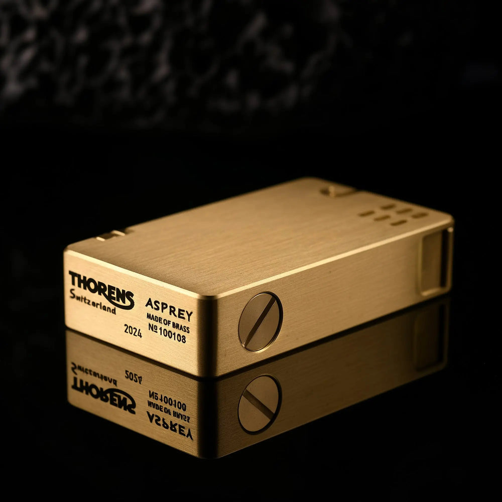 The bottom of a brass ASPREY lighter showing the Thorens Switzerland logo, "Made of Brass" engraving, and a unique serial number on a reflective surface.