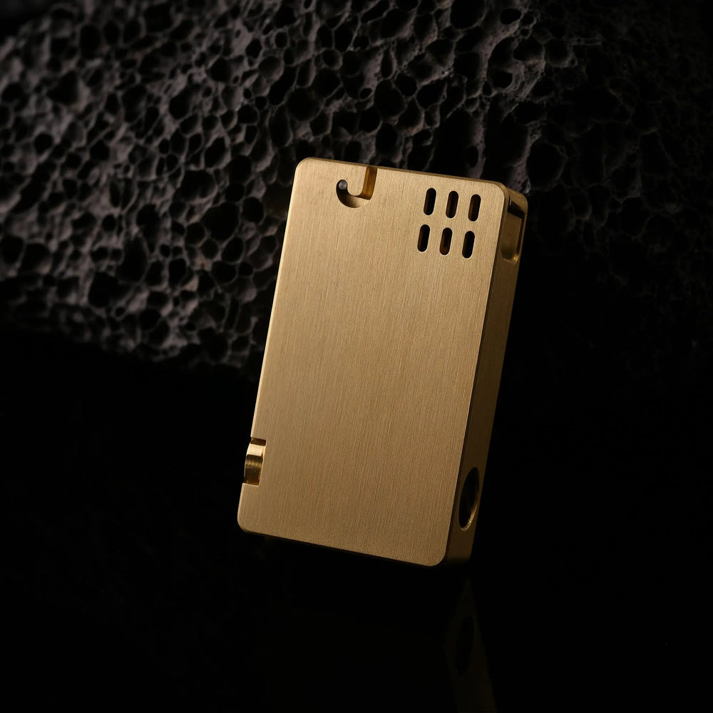 An ASPREY lighter with a textured brass surface and vertical vents, leaning against a dark volcanic rock backdrop for a refined EDC aesthetic.