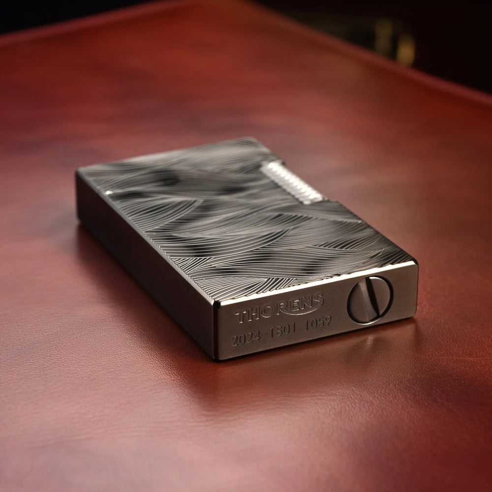 A close-up view of the Aqua Rhythm black lighter's base, showing the official Thorens logo and serial number engraved on the dark brass body.