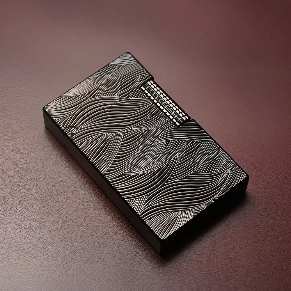 A Thorens Aqua Rhythm black lighter featuring high-contrast silver wave engravings, resting on a textured dark leather surface to highlight its refined EDC aesthetic.