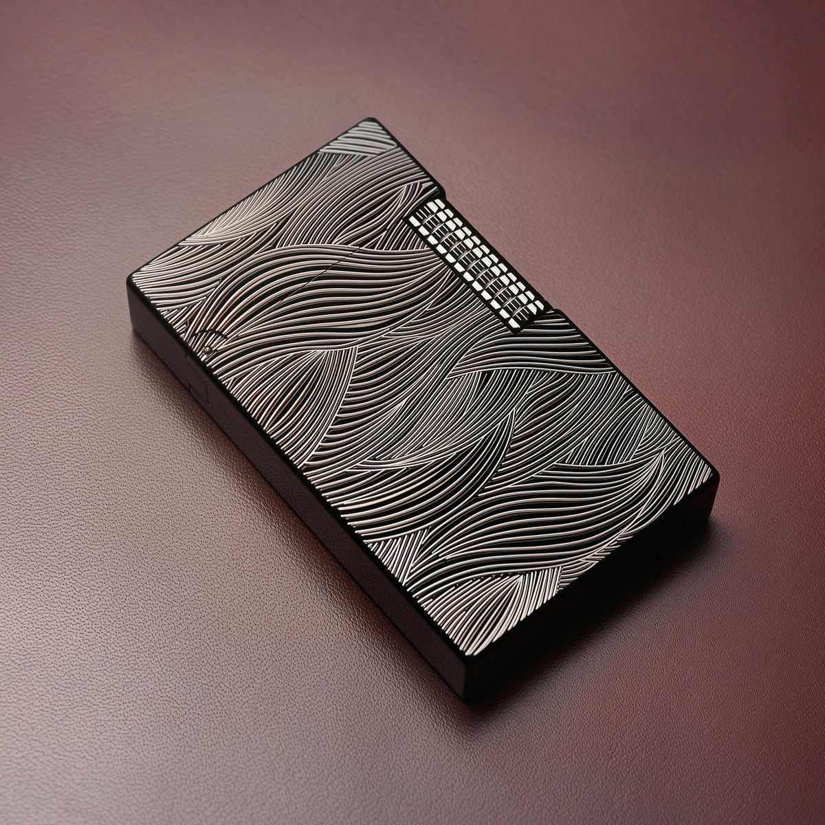 A Thorens Aqua Rhythm black lighter featuring high-contrast silver wave engravings, resting on a textured dark leather surface to highlight its refined EDC aesthetic.