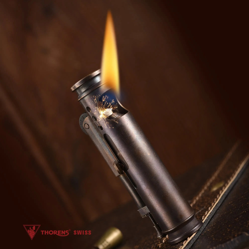Lit glossy Thorens Battle Soul trench lighter with visible wick flame against a warm wood background
