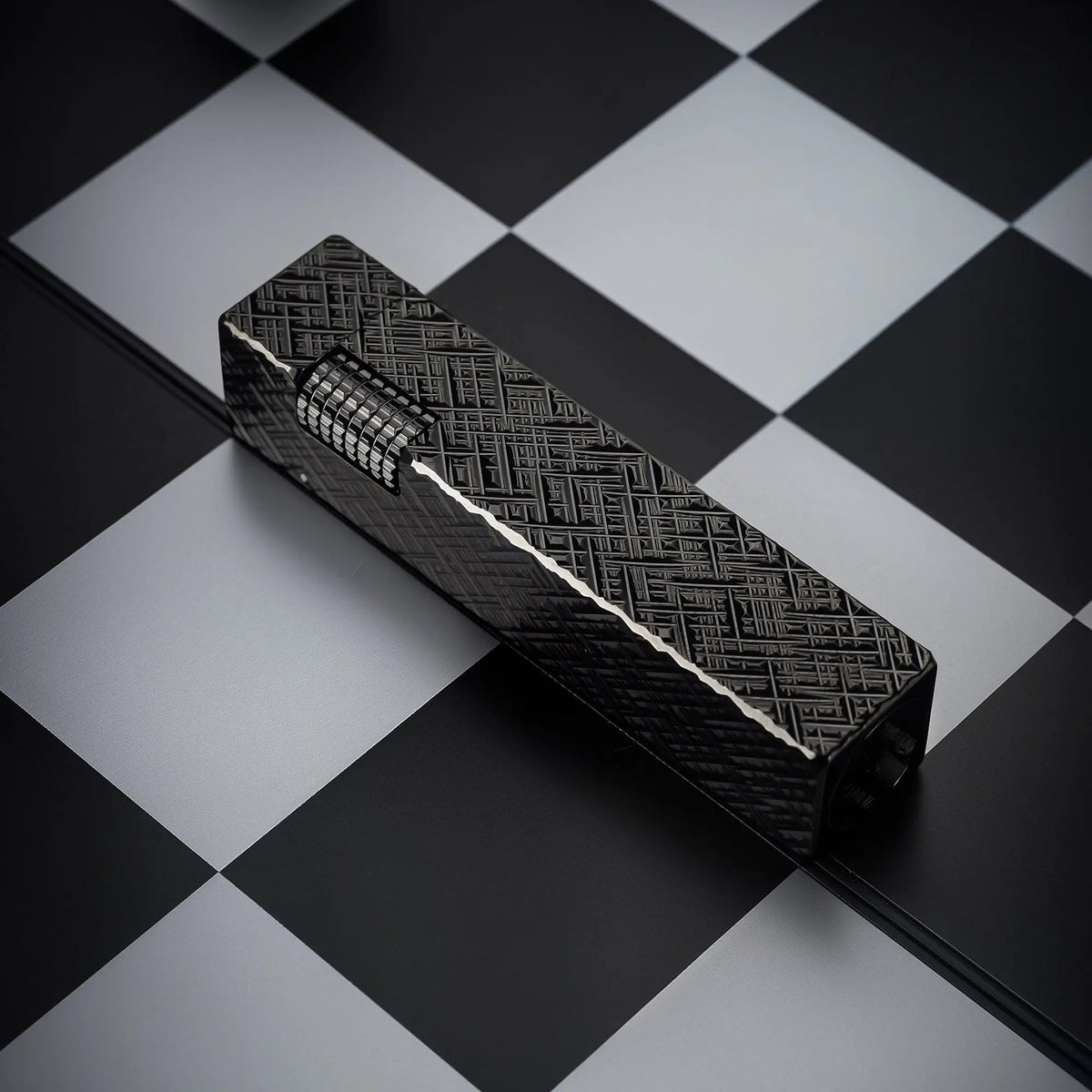 Black carved Thorens rectangular side-slip lighter shown in an angled closed view, featuring an engraved geometric texture and exposed side ignition wheel on a black and white checkered surface