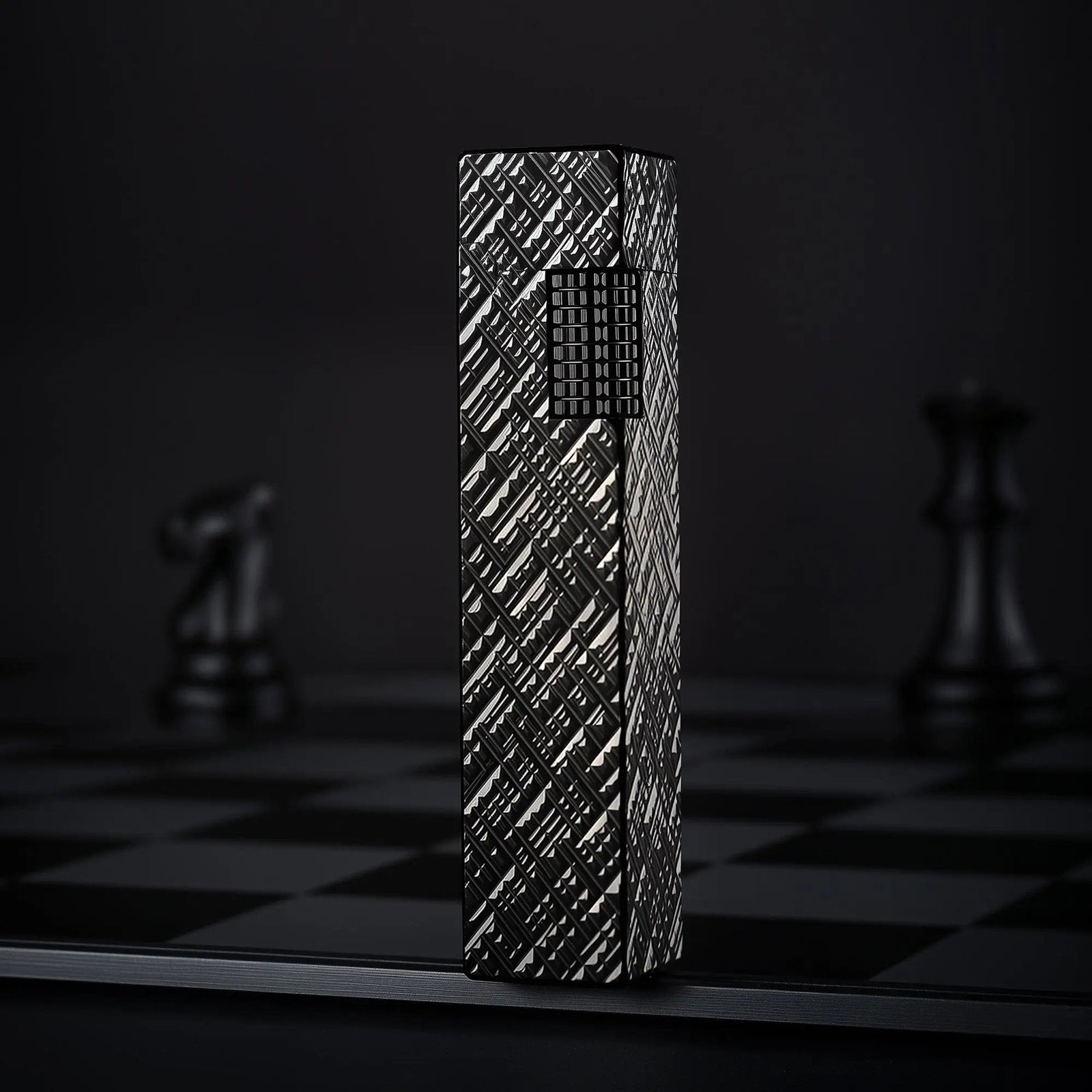 Black carved Thorens rectangular side-slip lighter standing upright in the closed position, featuring an engraved geometric texture and exposed side ignition wheel against a dark checkered background