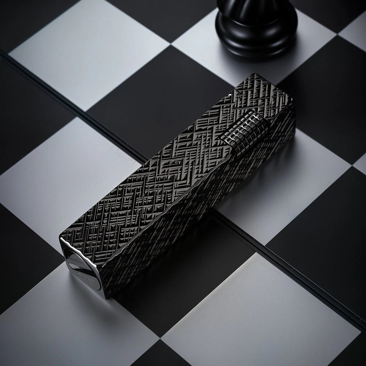 Black carved Thorens rectangular side-slip lighter with an engraved geometric texture and exposed ignition wheel, placed diagonally on a black and white checkered surface