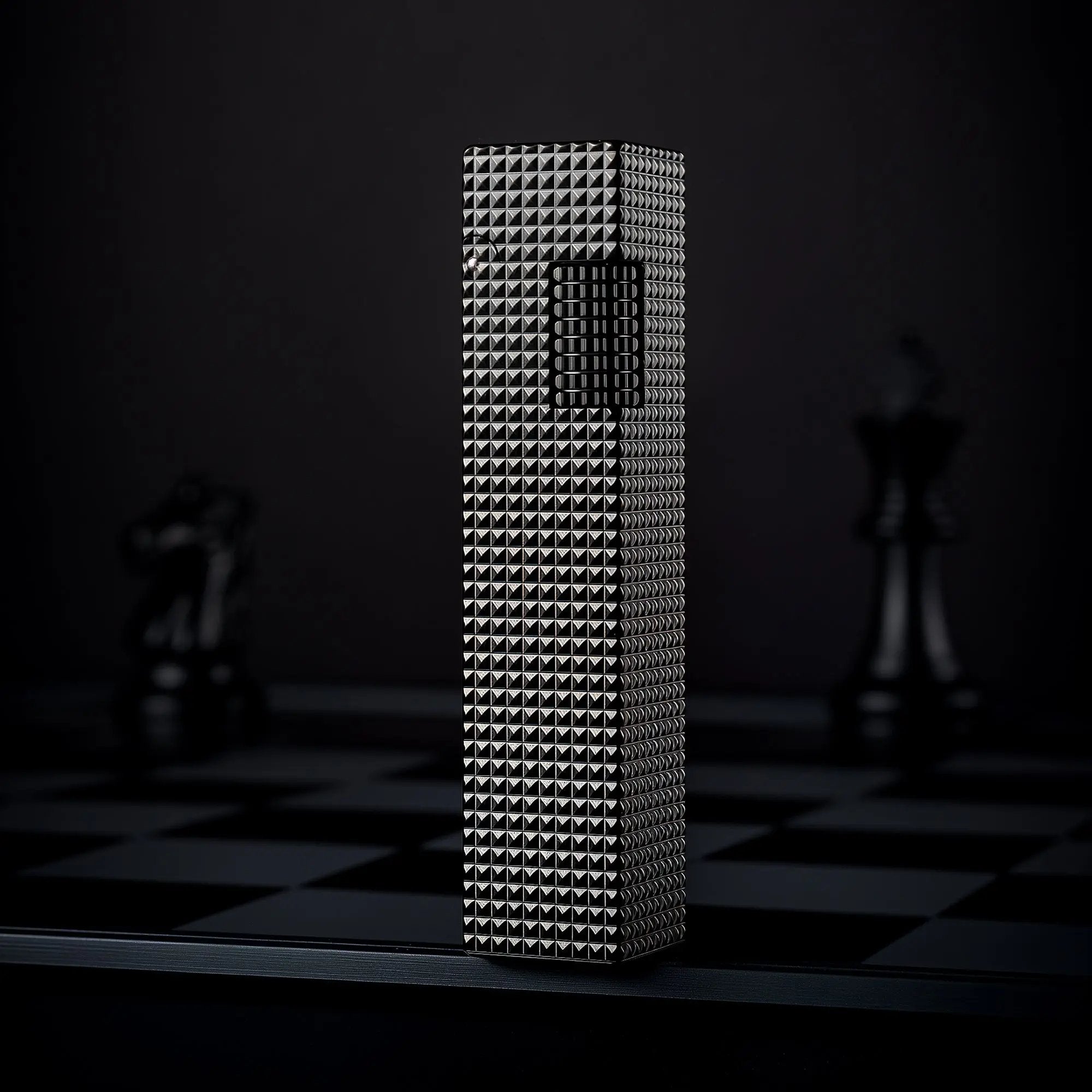 Black small square textured Thorens side-slip rectangular lighter standing upright on a dark checkerboard surface