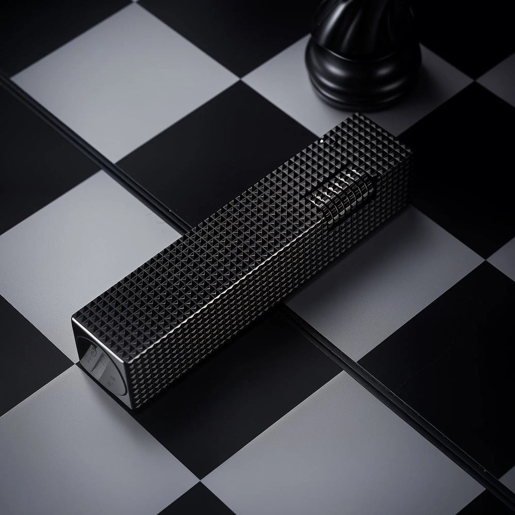 Angled detail view of a black small square textured Thorens side-slip rectangular lighter on a black and white checkerboard surface