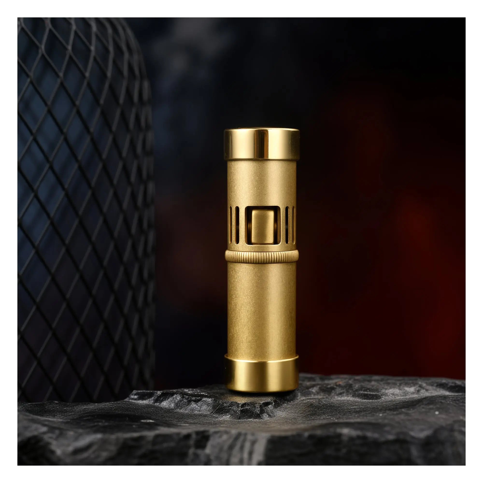 A Thorens Blaze Capsule lighter with a weathered vintage brass finish and polished gold-tone caps, standing upright on a dark, textured stone surface.