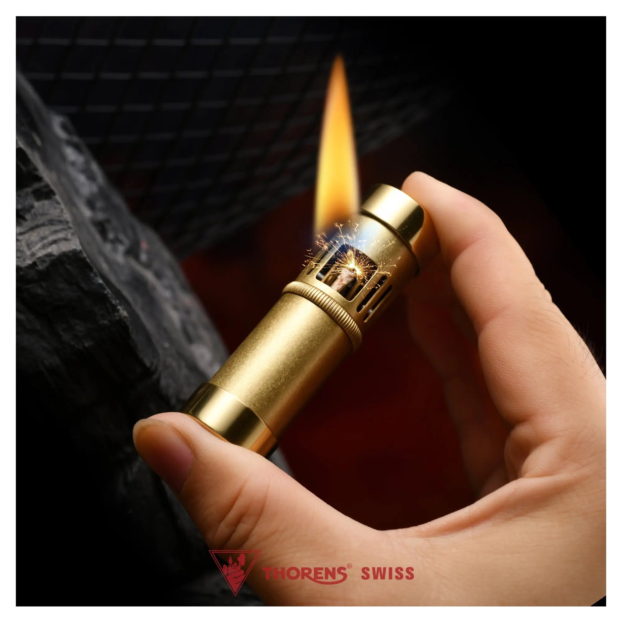 A hand-held Thorens Blaze Capsule lighter in vintage brass, shown during ignition with sparks and a steady flame, highlighting its ergonomic cylindrical design and industrial Swiss aesthetic.