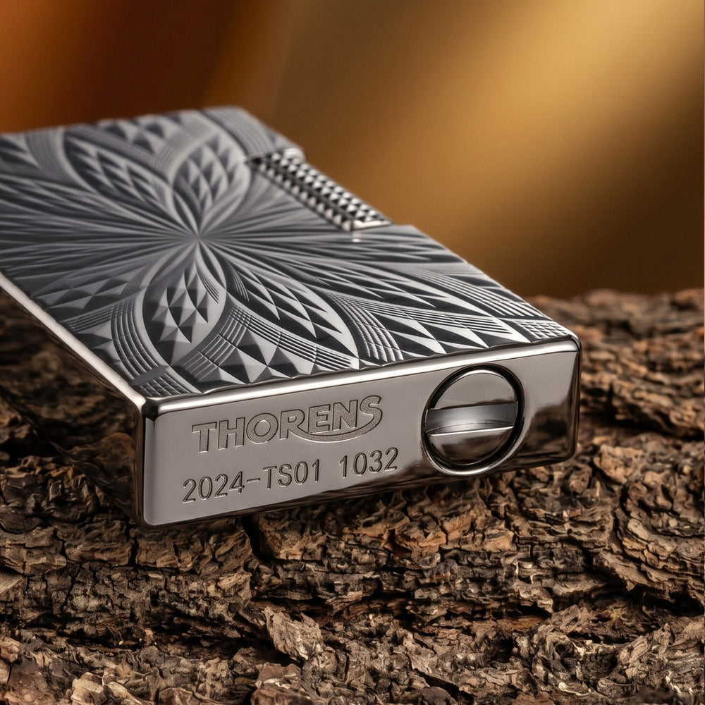 A Thorens Blooming Radiance black lighter with a geometric floral engraving, resting on a red leather surface to highlight its mechanical precision and brass craftsmanship.