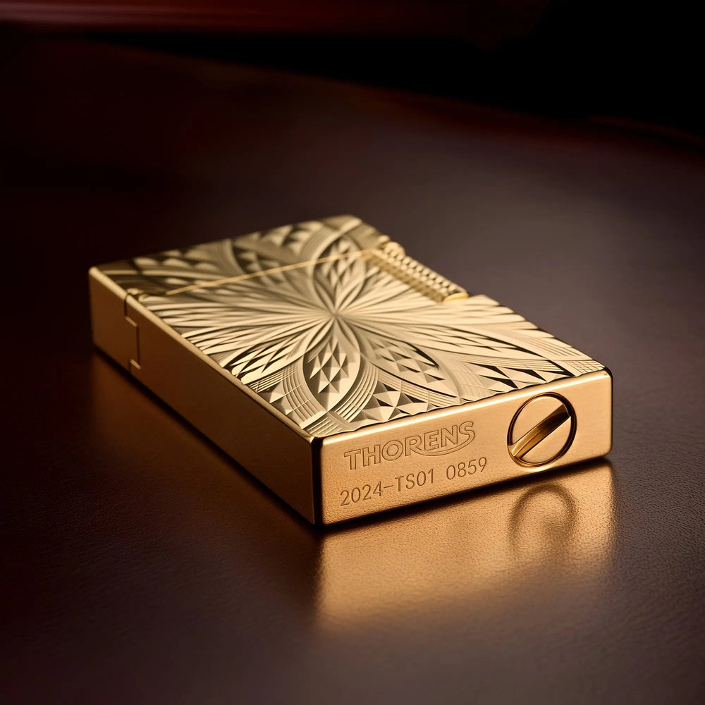An ignited Thorens Blooming Radiance gold brass lighter with its open lid, showing a warm flame and subtle mechanical sparks against the intricately engraved symmetrical floral pattern.