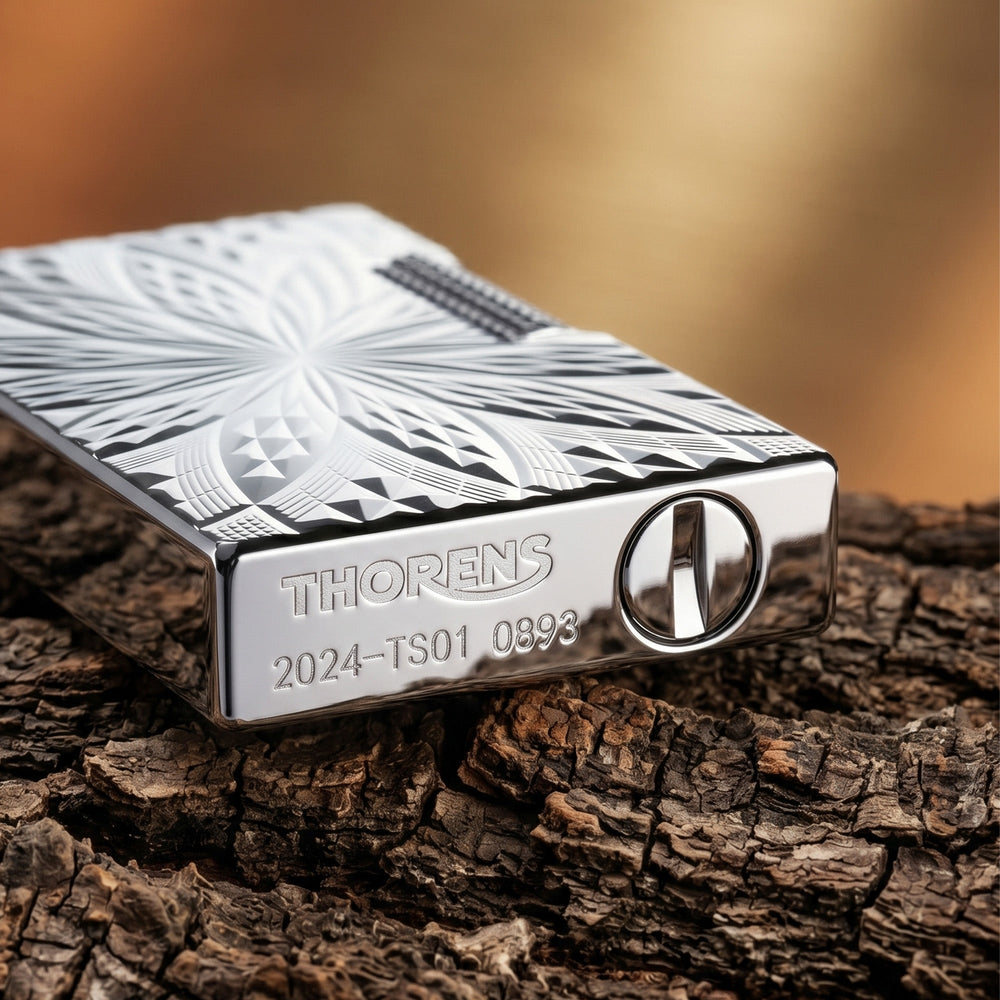A Thorens Blooming Radiance silver-plated lighter resting on a dark leather surface, highlighting the crisp, deep-etched floral geometry and brilliant metallic luster.