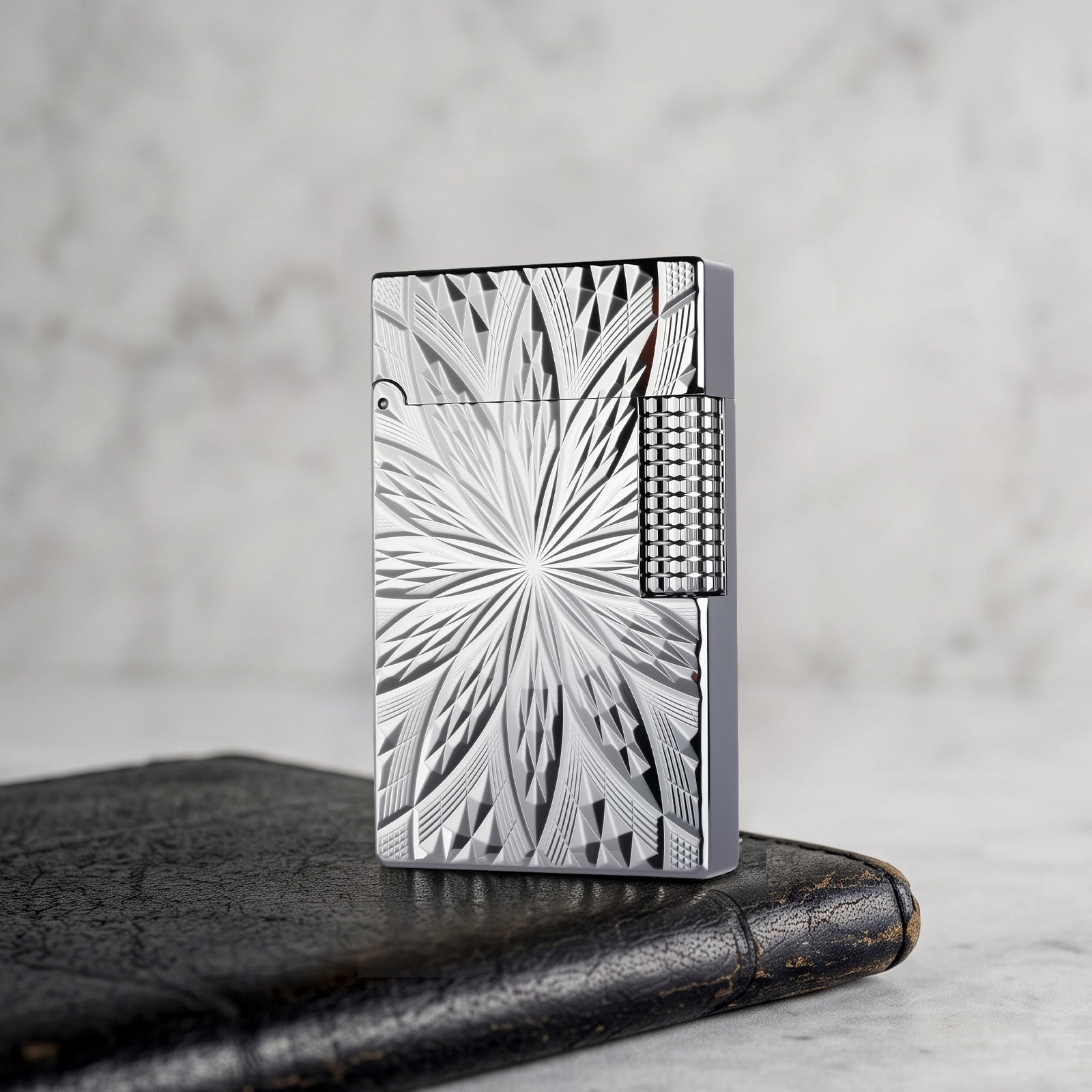 A Thorens Blooming Radiance silver-plated lighter resting on a dark leather surface, highlighting the crisp, deep-etched floral geometry and brilliant metallic luster.