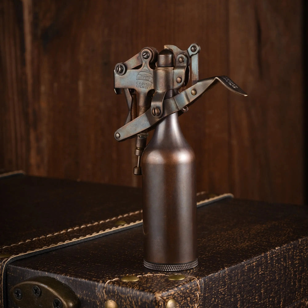 A glossy bronze Capitol Table Lighter standing on a vintage leather trunk, showcasing its unique mechanical lever system and refined heritage craftsmanship.