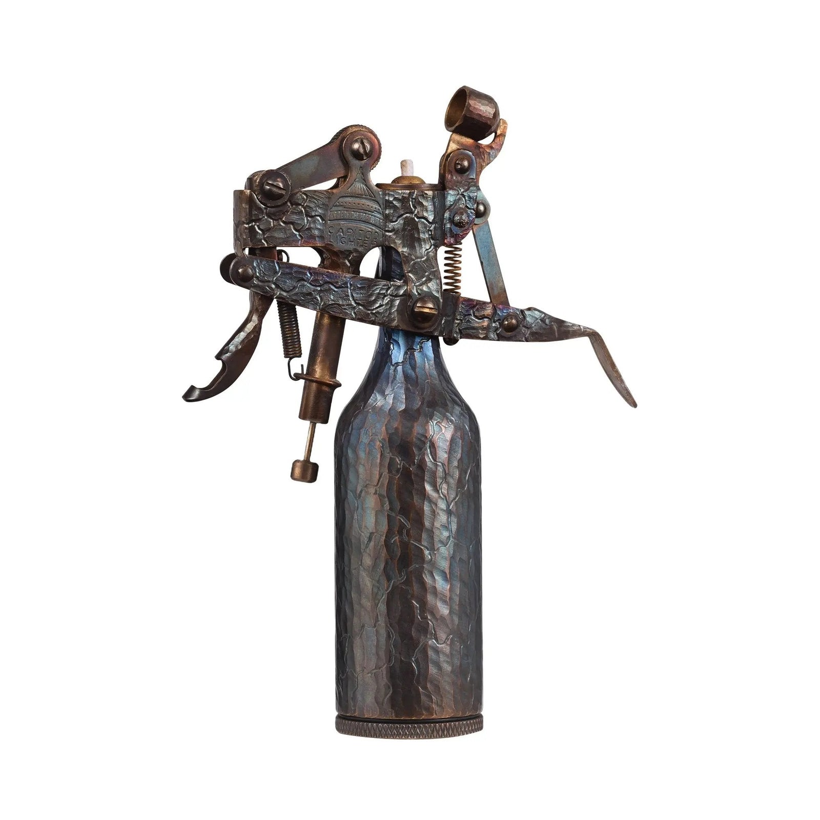 An upright Capitol Table Lighter showcasing a hand-carved "cracked" texture on its brass body, featuring an iridescent blue and bronze patina against a white background.