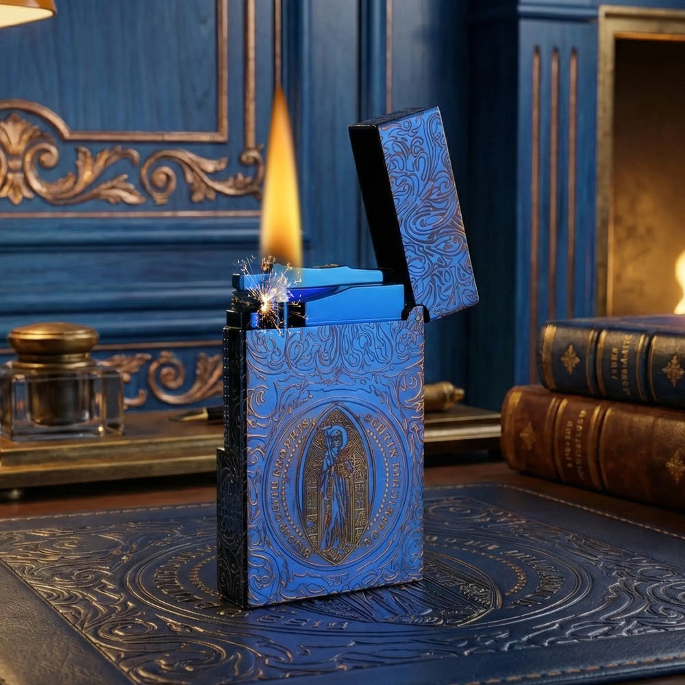 An open, ignited Constantine Midnight Blue Sigil lighter stands vertically, showcasing its detailed gothic engravings and prominent religious sigil against a dark, blue-lit background with a large cocktail glass.