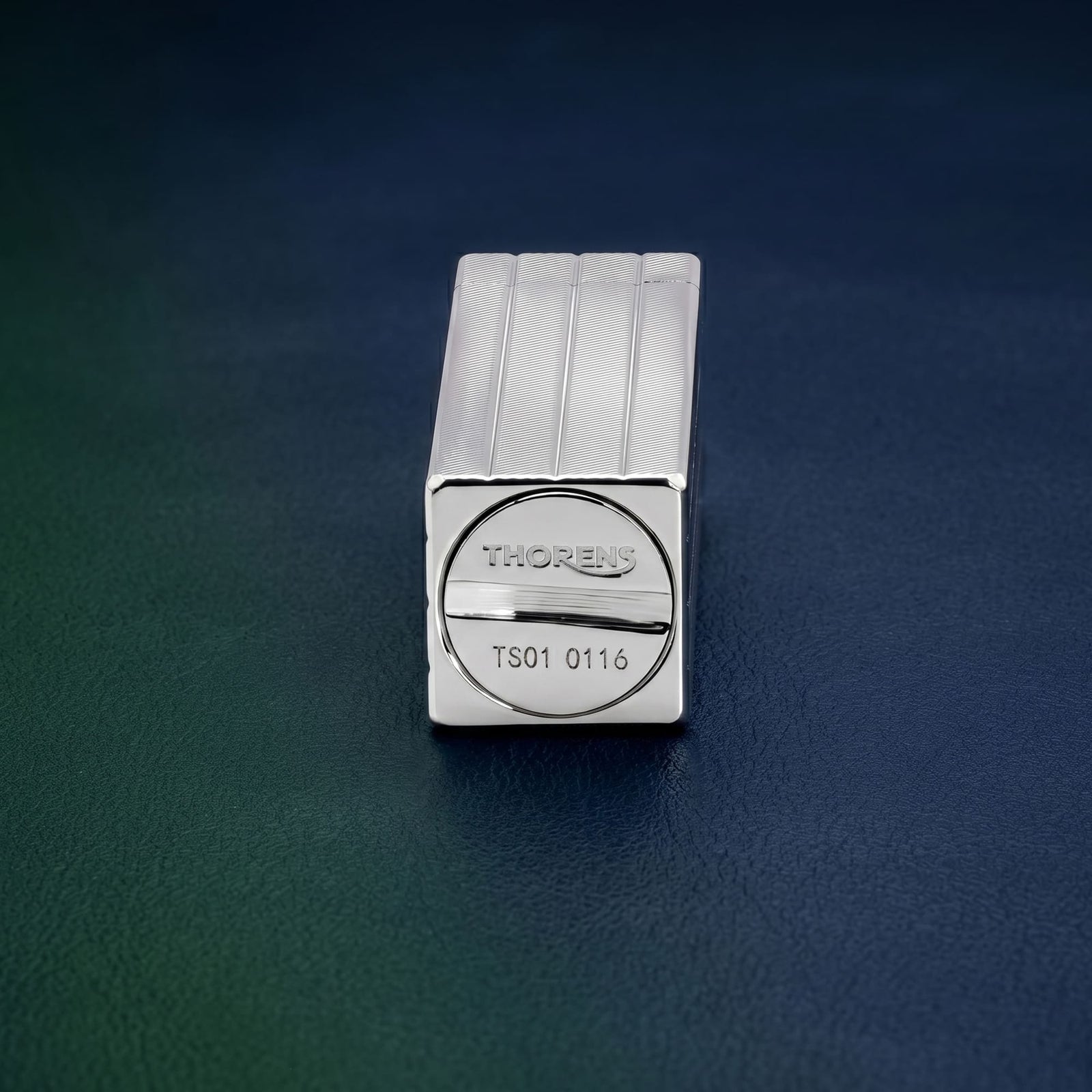 Thorens rectangular lighter in silver shown from the base, highlighting engraved logo plate, diagonal textured brass surface, and clean geometric form.