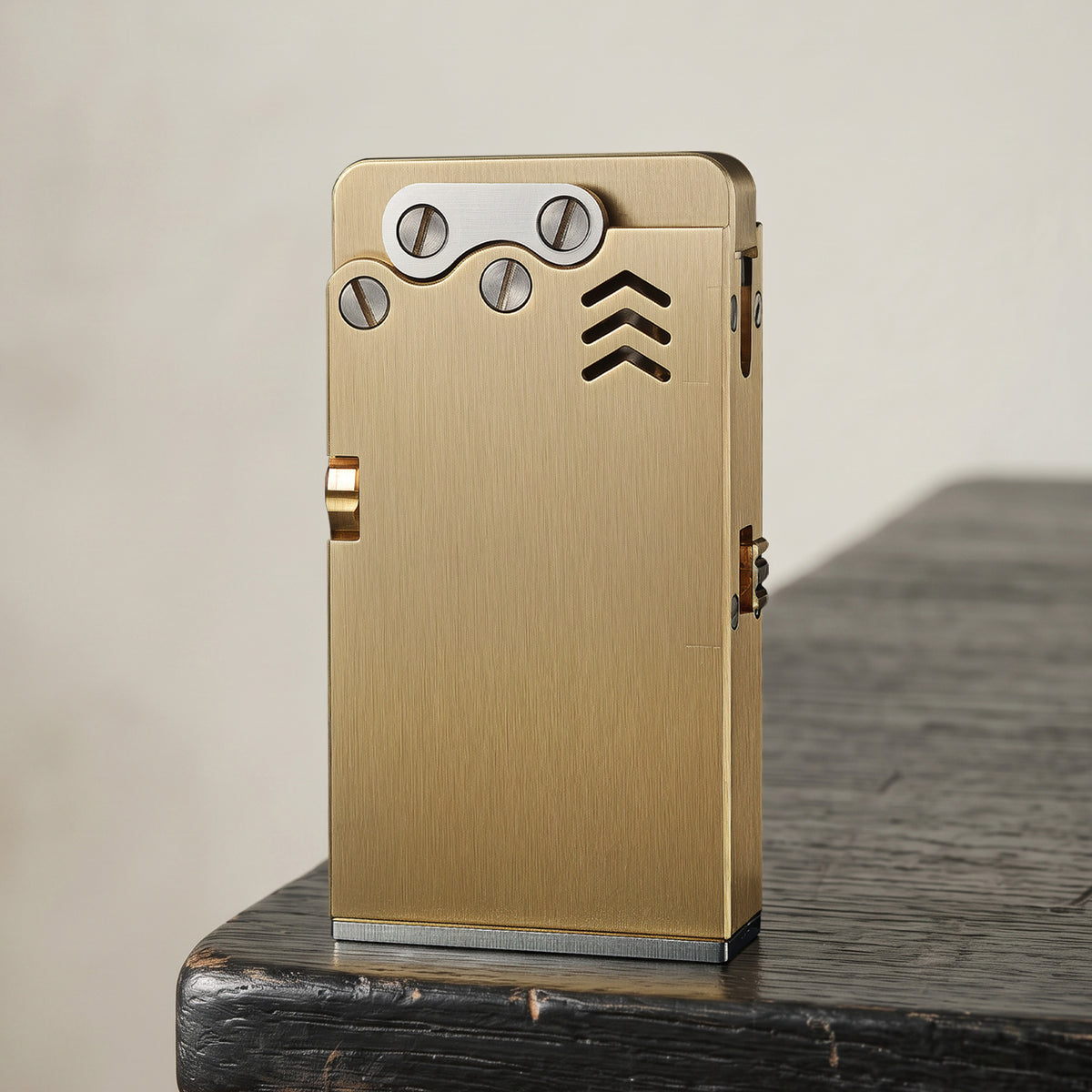 Thorens Ejection Lighter in brushed brass finish resting closed on a chessboard surface, showing engraved vents and precision mechanical construction.