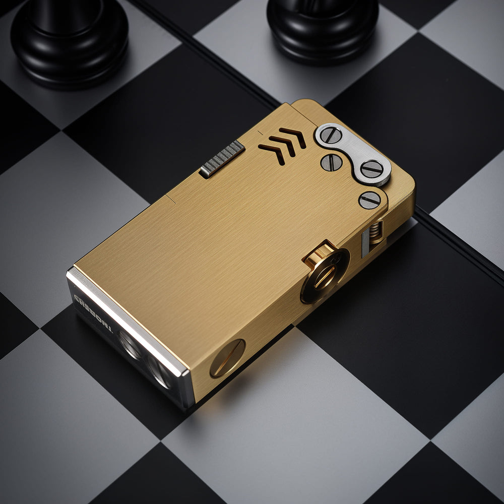 Thorens Ejection Lighter in brushed brass finish shown closed on a chessboard surface, highlighting side ignition slider and precision mechanical components.