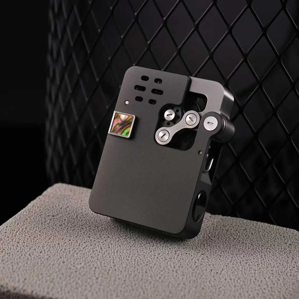 A sleek, matte black Thorens Ejection lighter featuring a "Hollowing Machine" industrial design, an abalone shell inlay accent, and a visible mechanical linkage system against a dark mesh background.