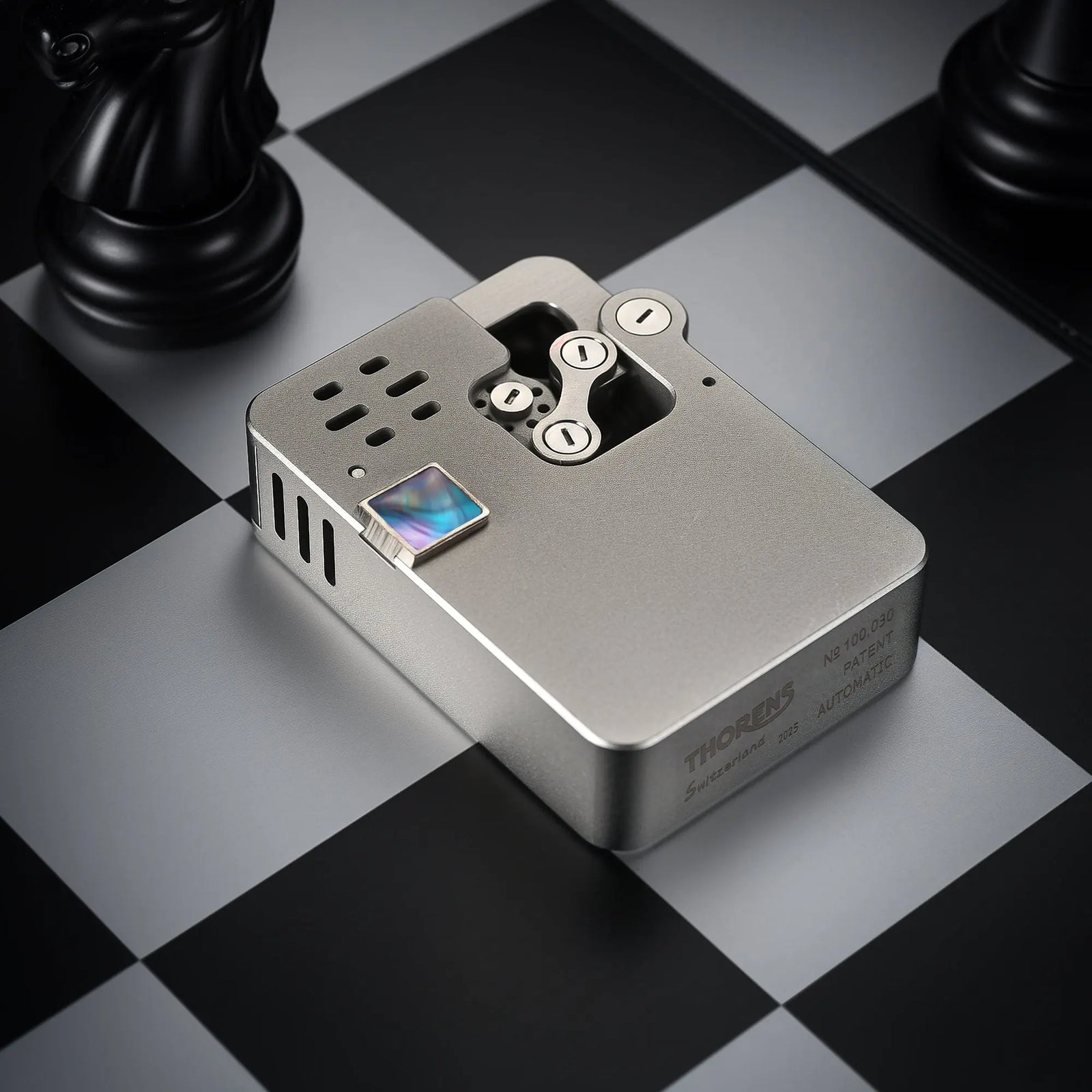 A side-angle view of the Ejection Lighter Hollowing Machine in brushed steel, featuring Thorens Swiss heritage engravings on a checkerboard.