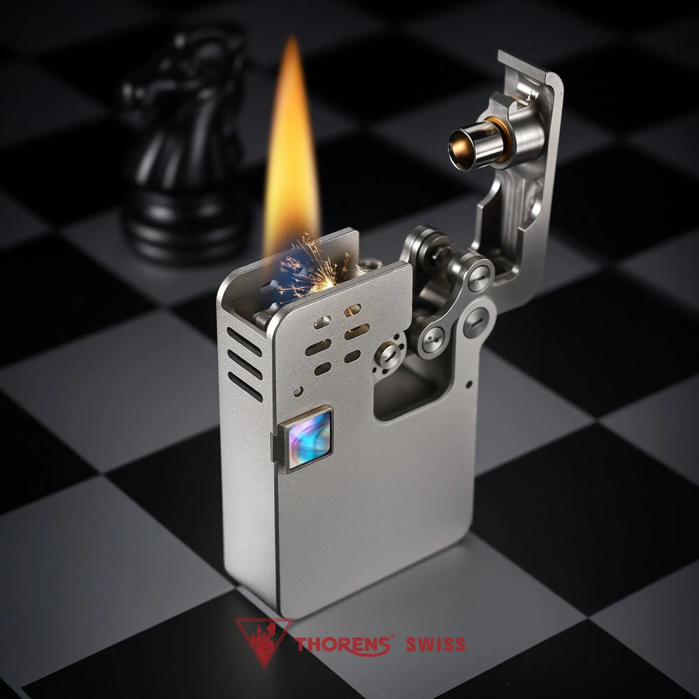 A brushed grey Ejection Lighter in an open, ignited state with a bright flame and visible sparks, showcasing its complex internal linkages and hollowing machine frame.
